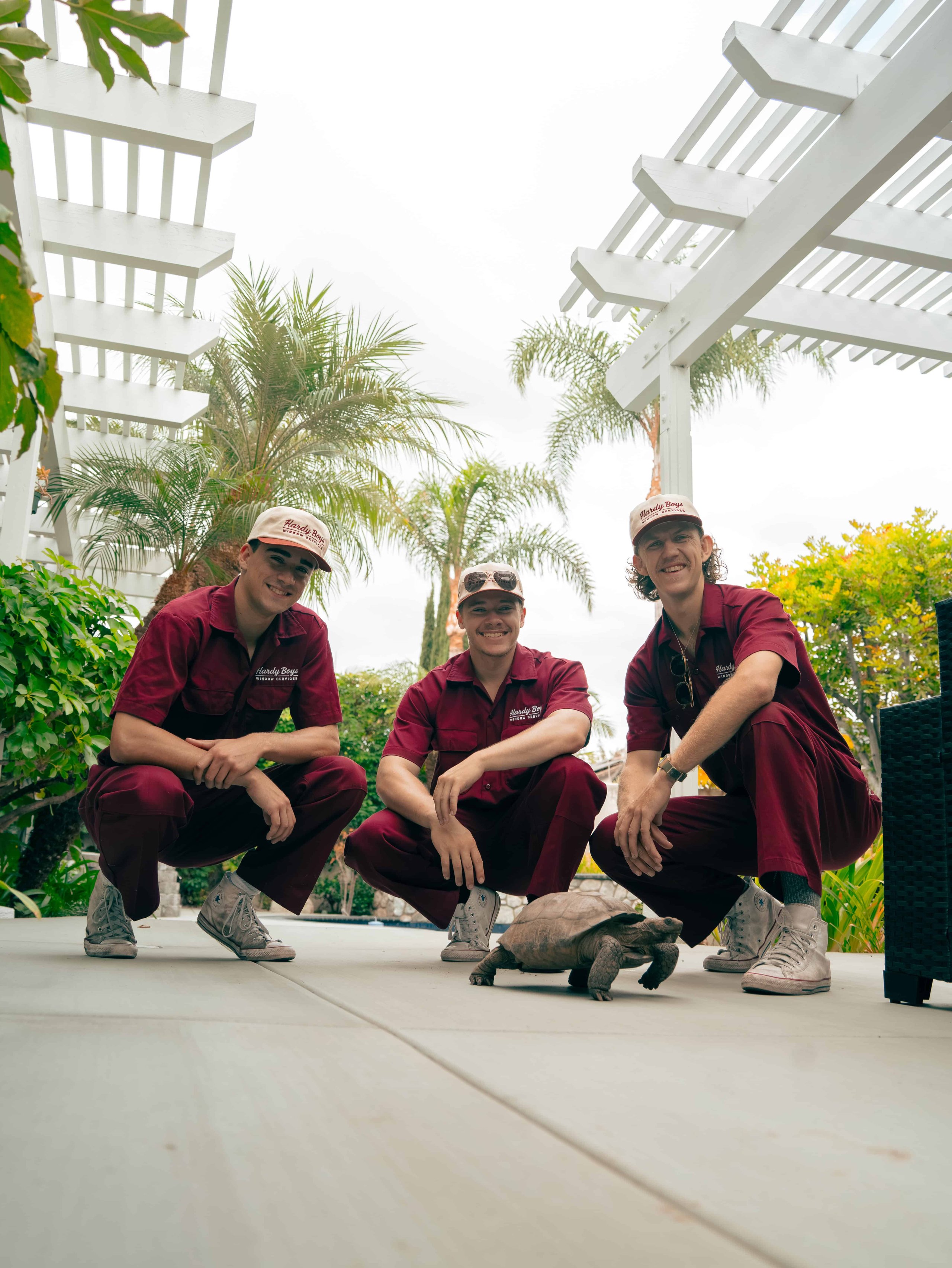 Workers in burgundy uniforms pose beneath a white pergola surrounded by tropical plants.
