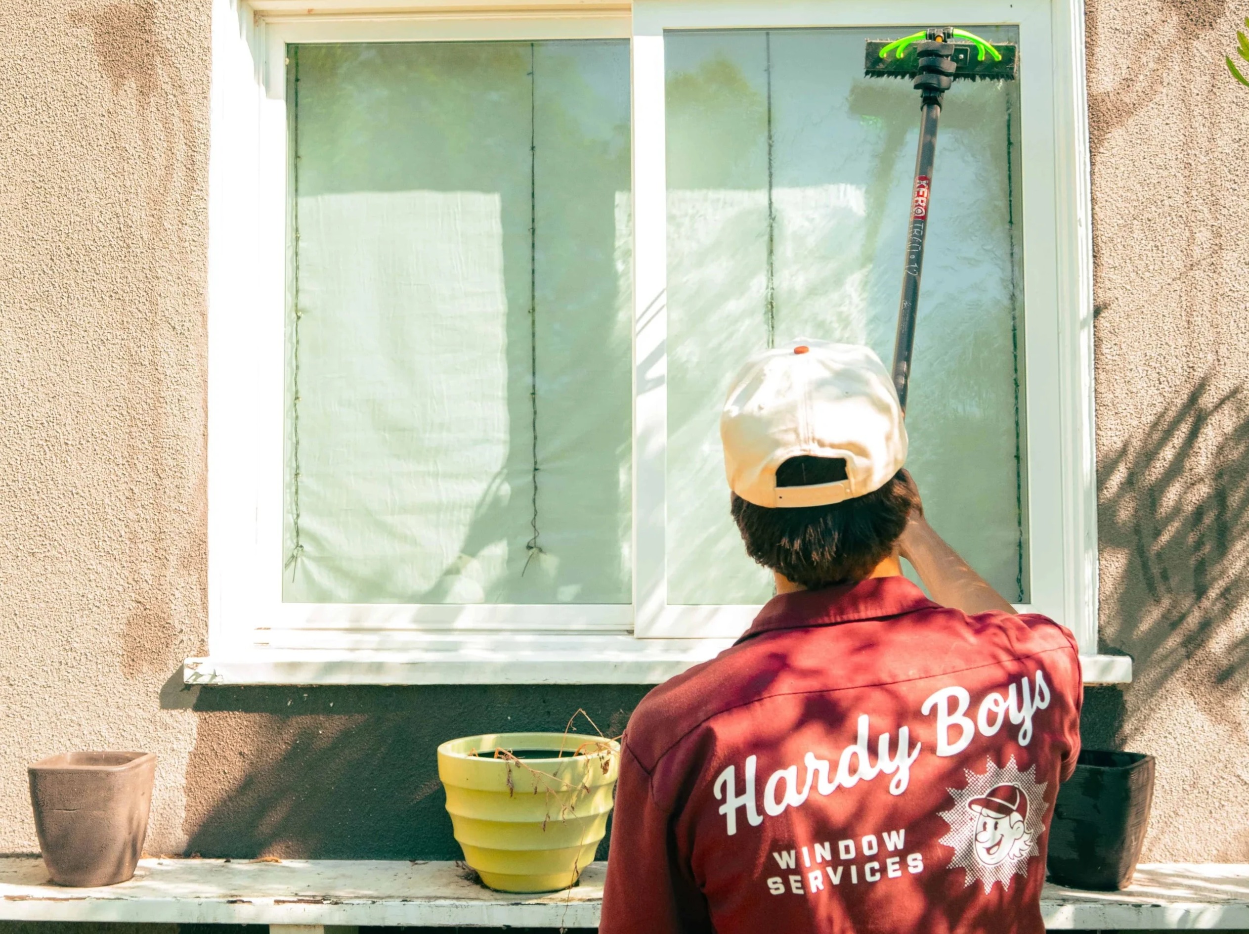 Window cleaner in a burgundy shirt uses a squeegee on a large window.