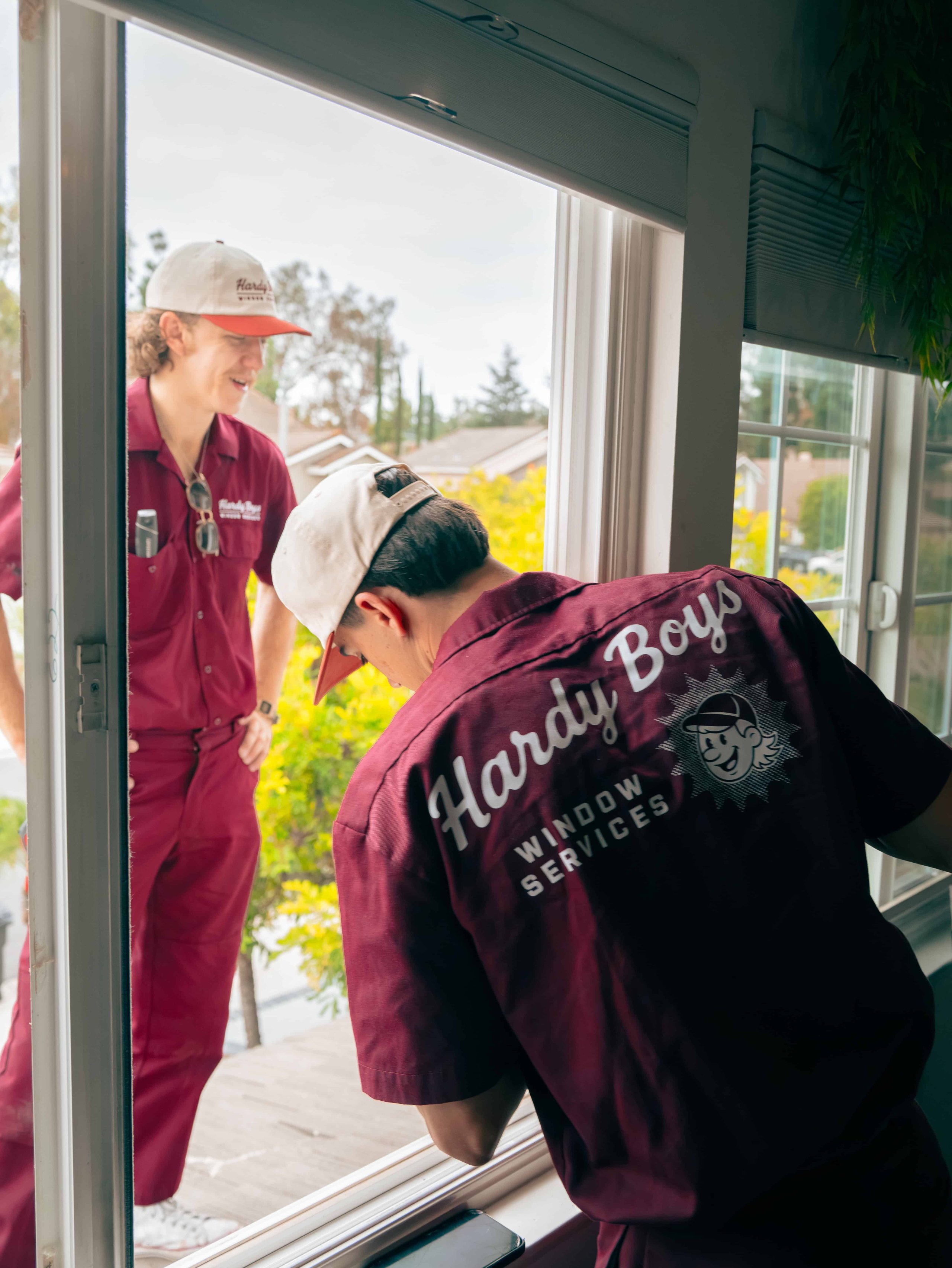 Two people in burgundy shirts stand by a bright window, one holding a clipboard.