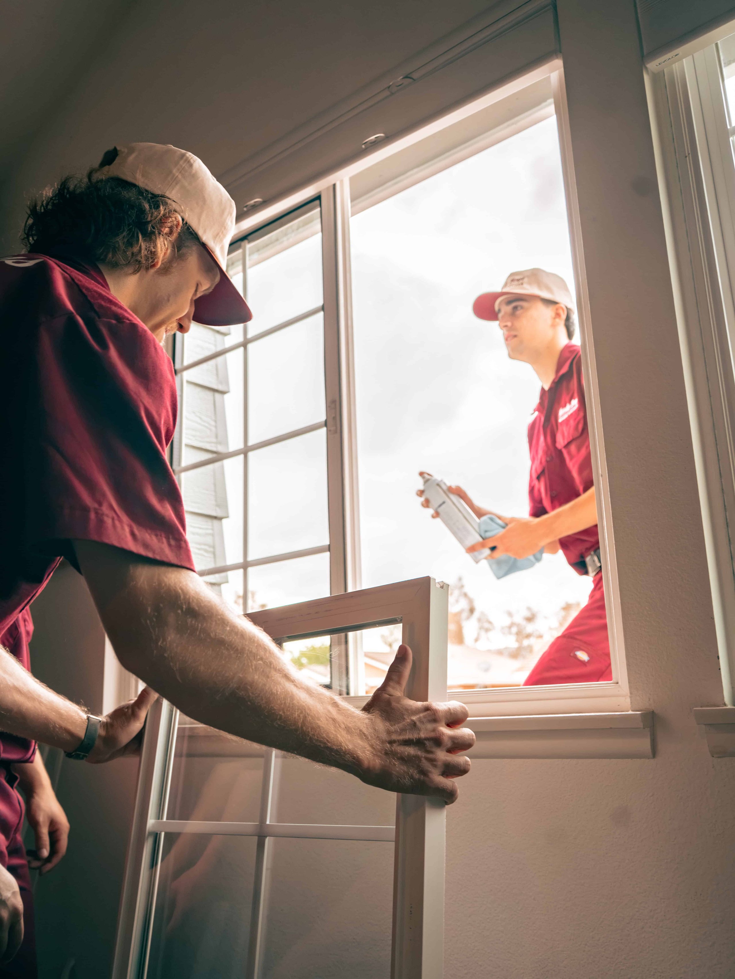 Sideways photo of a bearded man in glasses and a burgundy shirt looking down by bright windows.