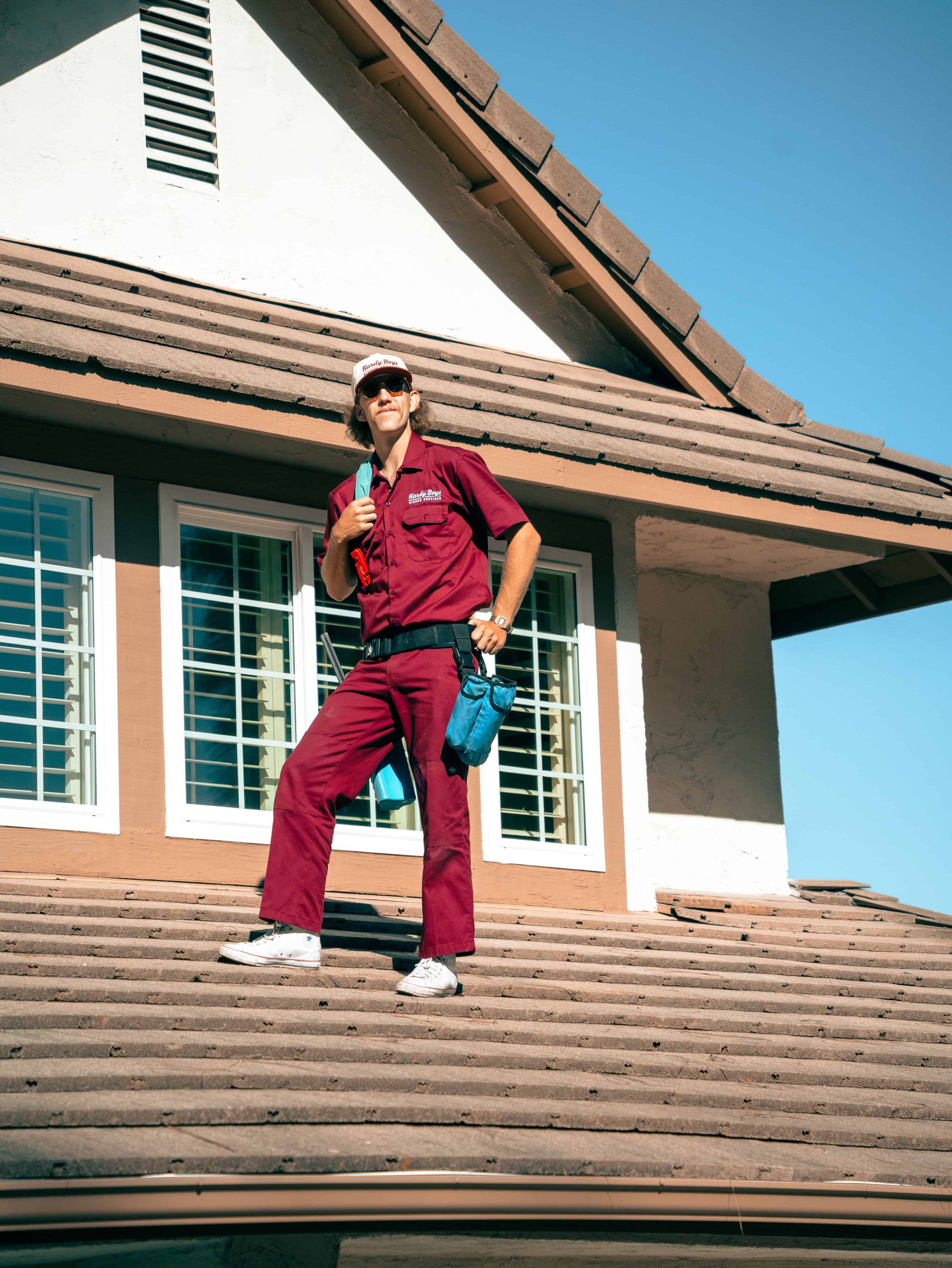 Person in burgundy work clothes and sunglasses standing on concrete steps outside a modern building.